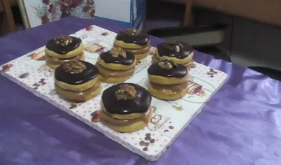 Готовое печенье остудите, сложите парами, прослаивая кремом. Затем каждую пару облейте глазурью и украсьте орехами.