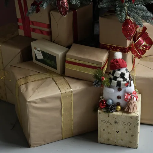 Упакованные подарки, лежащие у елки, которая оформлена в русском стиле.