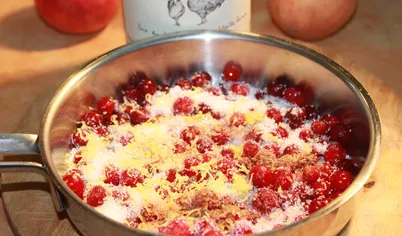Приготовить соус. В емкость, в которой будут готовиться яблоки, выложить клюкву, сахар, цедру лимона, корицу и влить вино. Поставить на огонь и, помешивая, довести до кипения.